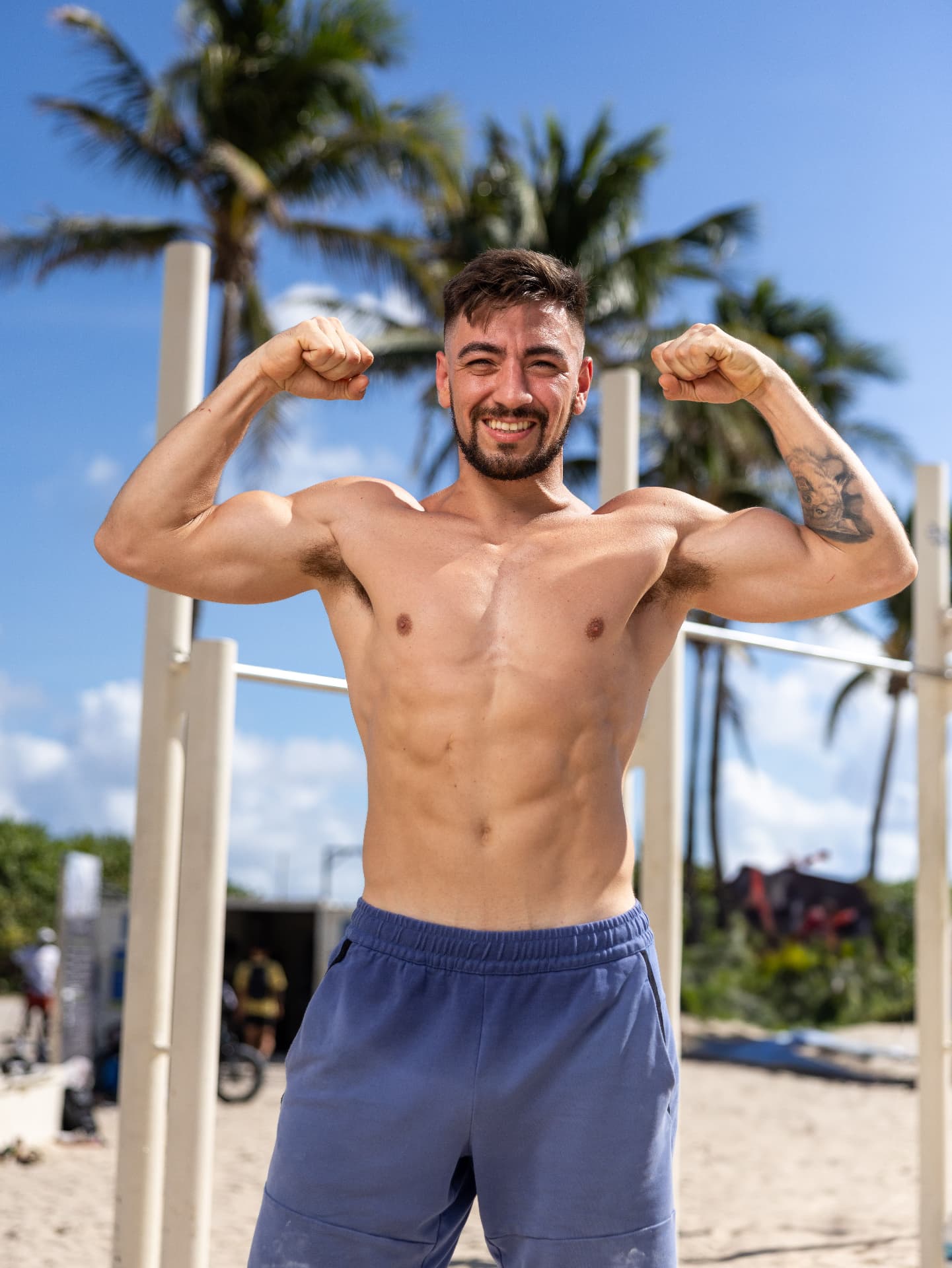 Male pro calisthenics athlete flexing at the beach bars